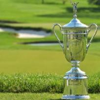 Ein großer, silberner Pokal steht auf einem gemähten Rasen vor dem Hintergrund eines Golfplatzes.